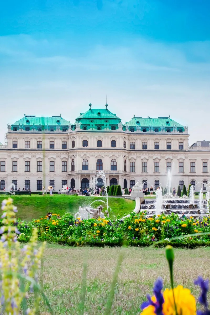 The Baroque yellow facade of Schönbrunn Palace and its formal gardens under a blue Vienna sky, Austria